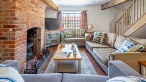 A cozy living room with a brick fireplace, a sofa set, a coffee table, and a television. - Angel Cottage, Great Walsingham, Norfolk (Walsingham)