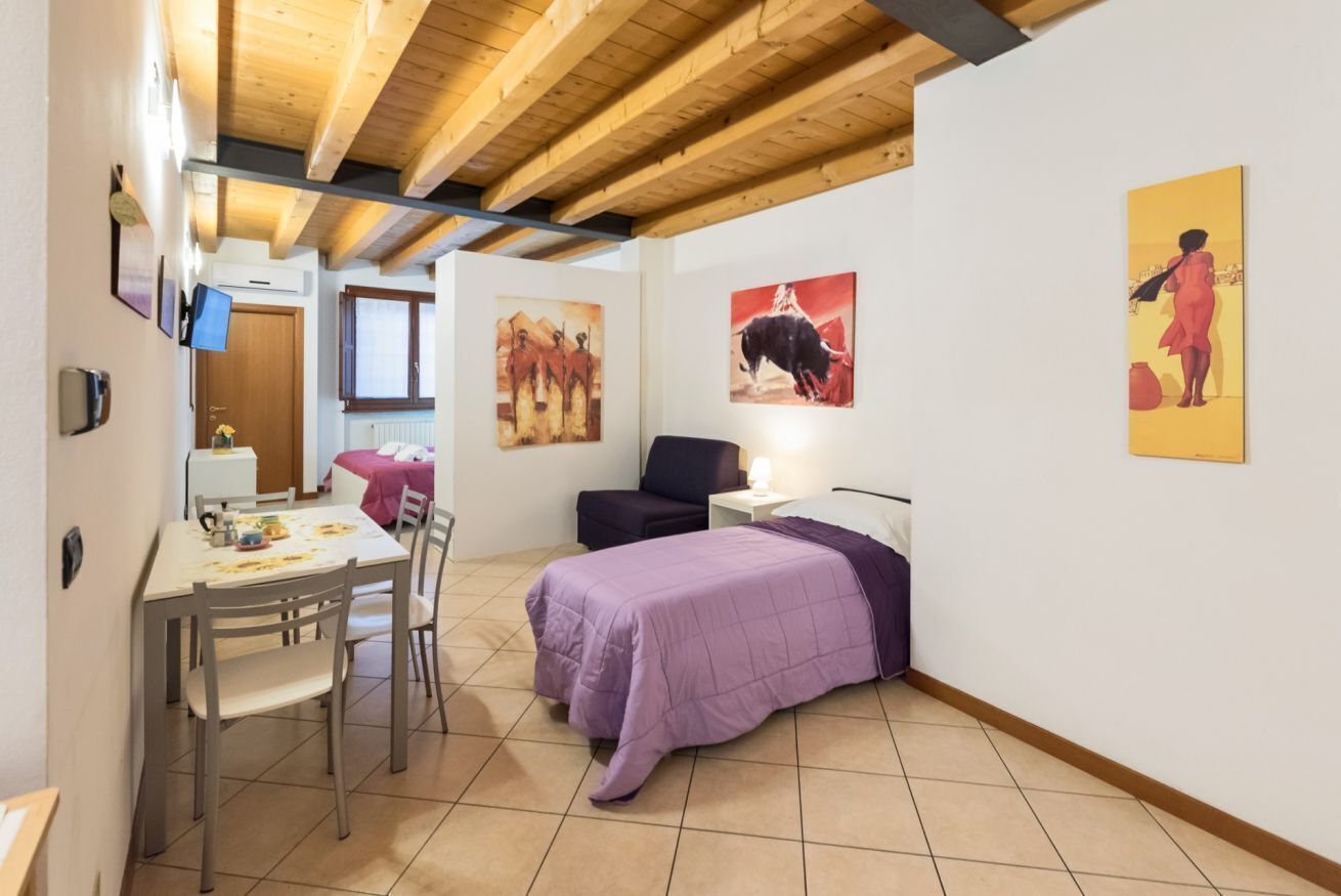 A room with a bed, a desk, and a chair. There are paintings on the walls.