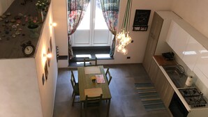 Una cucina compatta con zona pranzo, una finestra ornata da tende floreali e una lavagna con scritte.
