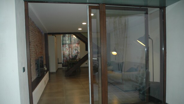Un interno moderno con una porta in vetro che conduce a una zona giorno, una scala e una parete in mattoni.
