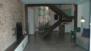 Un soggiorno moderno con una parete in mattoni, una scala che conduce a una zona pranzo e un televisore a schermo piatto montato al muro.