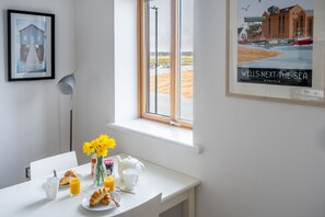 A breakfast table with croissants, a vase of flowers, and a framed picture of a coastal scene. - Quayside Lookout, Wells-next-the-Sea, Norfolk (Wells-next-the-Sea)