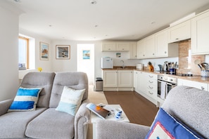 A modern living room with a sofa, a coffee table, and a kitchen in the background. - Quayside Lookout, Wells-next-the-Sea, Norfolk (Wells-next-the-Sea)