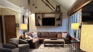 Una sala de estar con un sofá modular, un sillón gris, una mesa de centro y un televisor montado en la pared.