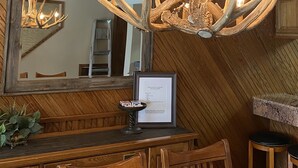 Un comedor de madera con una araña hecha de astas, un espejo grande y un menú enmarcado en la pared.