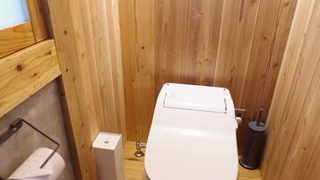 A wooden-paneled bathroom with a toilet, a toilet paper holder, and a trash can.