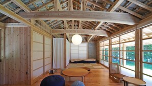 Una habitación amplia con pisos de madera, esteras de tatami, techo bajo y ventanas grandes.
