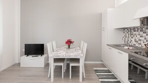 A compact kitchen with white cabinets, a tiled backsplash, and a dining area with a table and chairs. - Appartamento con due camere a 1 km da Piazza Erbe (Verona)