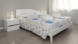 A neatly made bed with a floral quilt, white bedding, and two bedside lamps. - Appartamento con due camere a 1 km da Piazza Erbe (Verona)