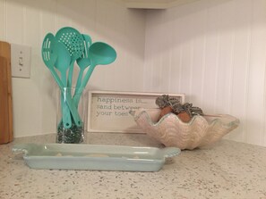 A kitchen counter with a teal-colored spatula set, a decorative bowl with starfish, and a framed inspirational quote. - 2BR Oasis • Dog Friendly • 5 min to Manasota Beach (Englewood)