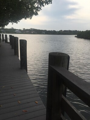 A wooden pier extending into calm water, with a tree overhead and distant houses on the shore. - 2BR Oasis • Dog Friendly • 5 min to Manasota Beach (Englewood)