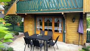 Et træhus med balkon, spisebord med stole og en lille have.