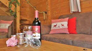 Et hyggeligt interiør i en hytte med træpaneler, en sofa med ternede puder, en vinflaske og dekorative glas på et træbord.