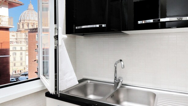 A kitchen with a stainless steel sink, black cabinets, and a window overlooking a cityscape with a dome building. - Beautiful apartment 100 meters from the center of Rome Vatican (Roma)