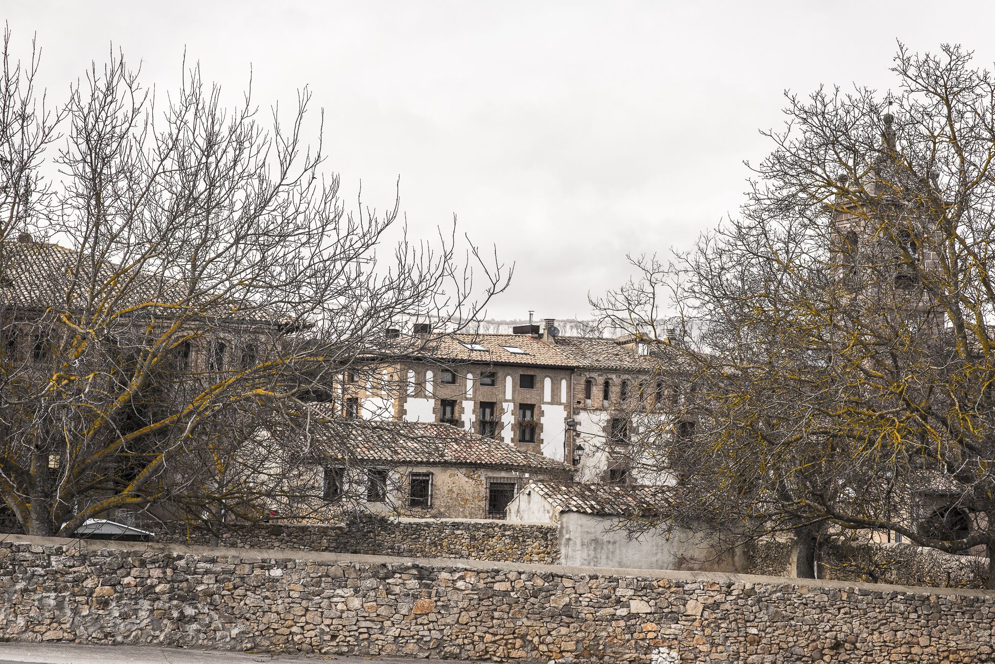 A historic building with a stone wall in front, featuring a traditional tiled roof and multiple windows.