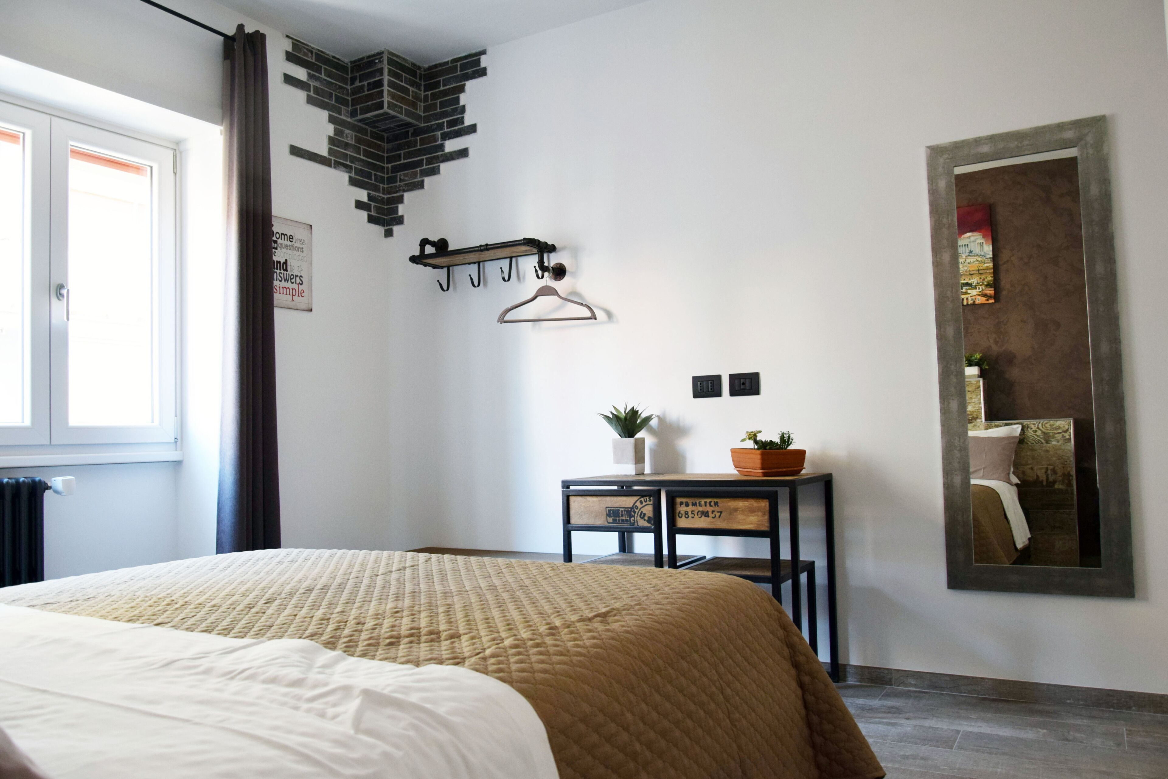 Un dormitorio con cama, una mesita con plantas, perchero y espejo en la pared.