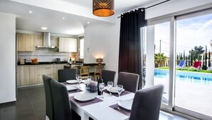 A dining area with a table set for four, a kitchen in the background, and a view of a swimming pool. - VALLESA - Modern villa with private pool near the beach and supermarkets (Calpe)