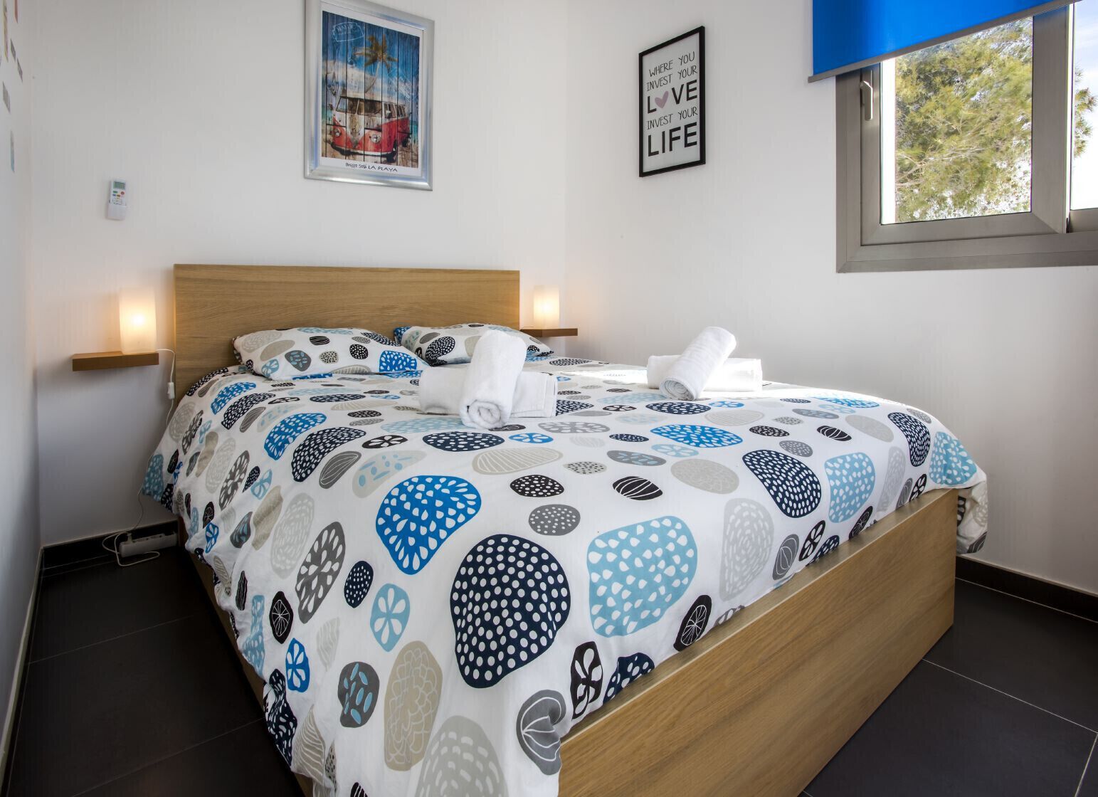 Een net opgemaakt bed met beddengoed met patroon, een houten hoofdbord en twee wandlampen.
