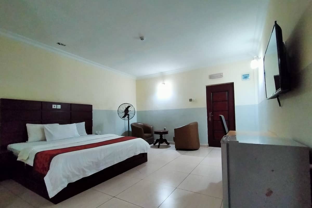 A hotel room with a bed, a desk, a chair, a fan, and a TV.