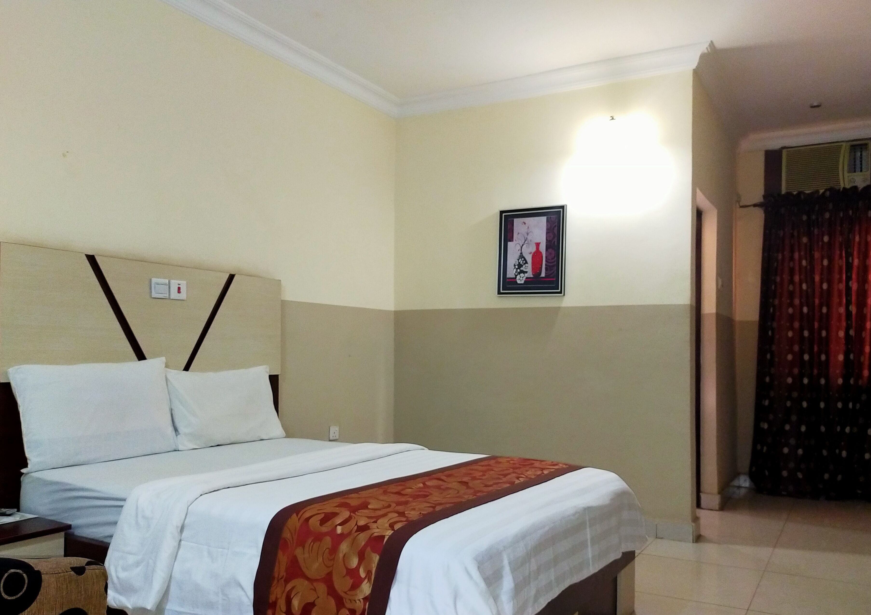 A hotel room with a bed, a nightstand, a framed picture on the wall, and a curtain.