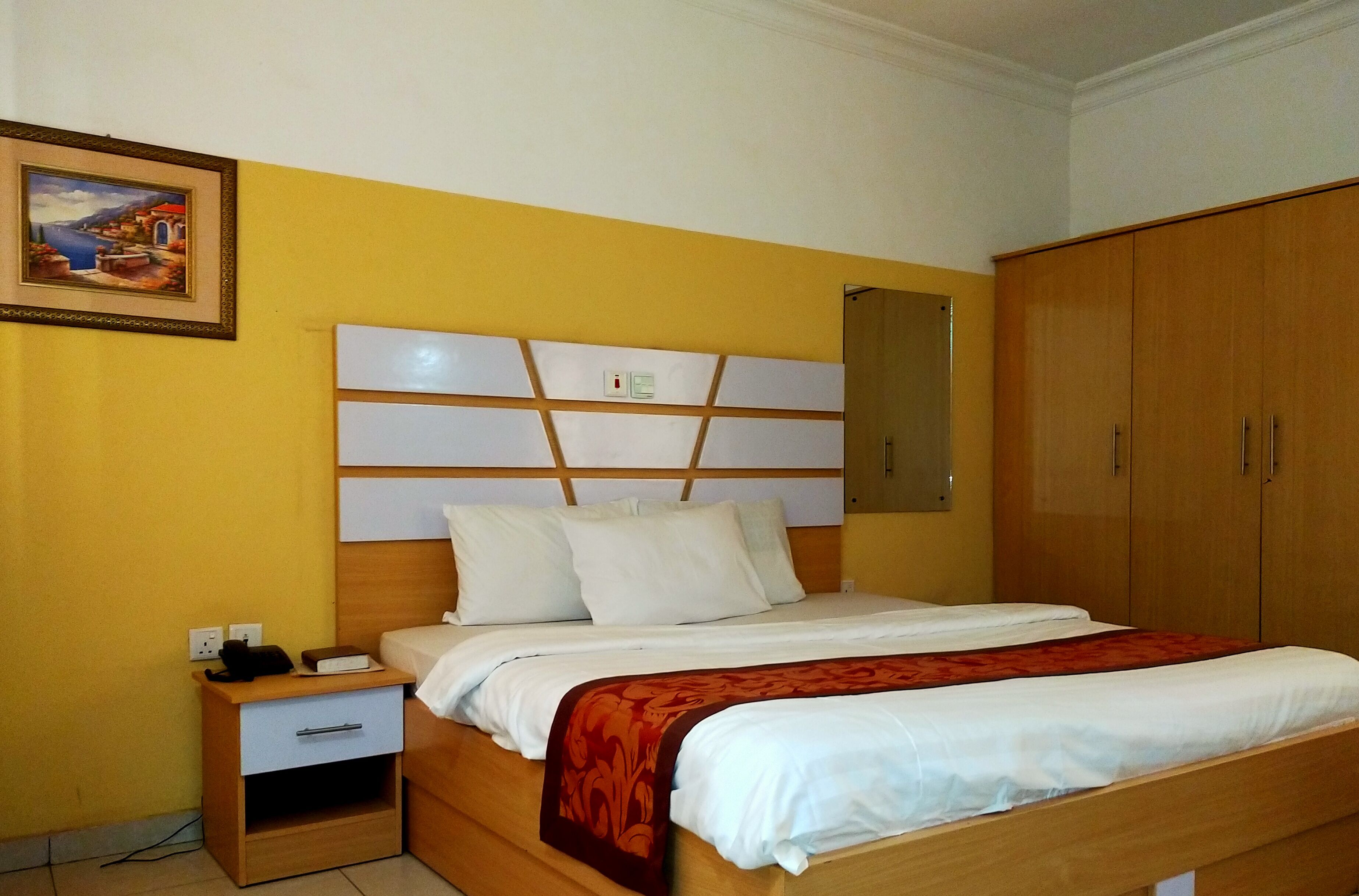 Una habitación de hotel con una cama, una mesita de noche, un armario de madera y un cuadro en la pared.
