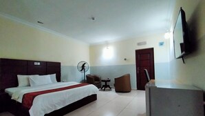 Une chambre d’hôtel équipée d’un lit, d’un bureau, d’une chaise, d’un ventilateur et d’une télévision.
