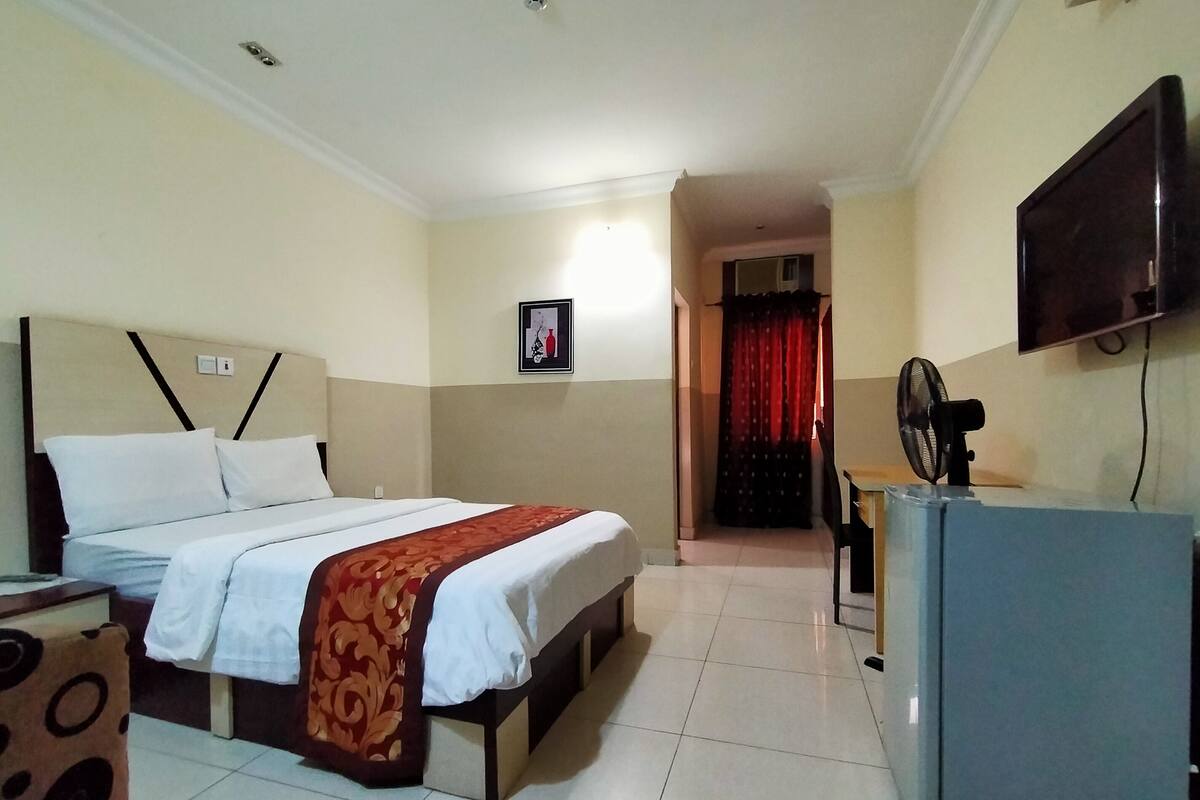 A hotel room with a bed, a desk, a television, and a fan.