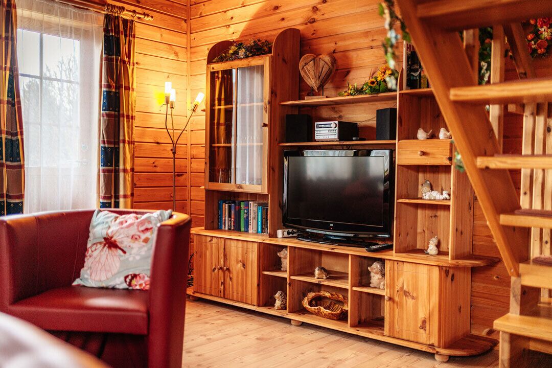 Ein gemütliches Holzhaus-Interieur mit Fernseher, Bücherregalen und einem roten Ledersessel.