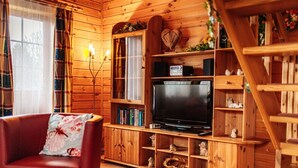 L’intérieur d’un chalet en bois chaleureux et accueillant, avec un téléviseur, des étagères à livres et un fauteuil en cuir rouge.