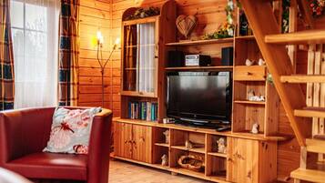 Ein gemütliches Holzhaus-Interieur mit Fernseher, Bücherregalen und einem roten Ledersessel.