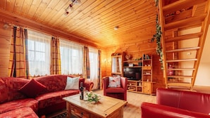L’intérieur chaleureux d’un chalet avec un plafond en bois, un canapé rouge, une table basse en bois et un téléviseur intégré dans un meuble de rangement en bois.