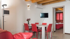 Una sala de estar moderna con un sofá rojo, una mesa de comedor con sillas rojas, un televisor de pantalla plana montado en la pared y una mesita con un jarrón de flores.