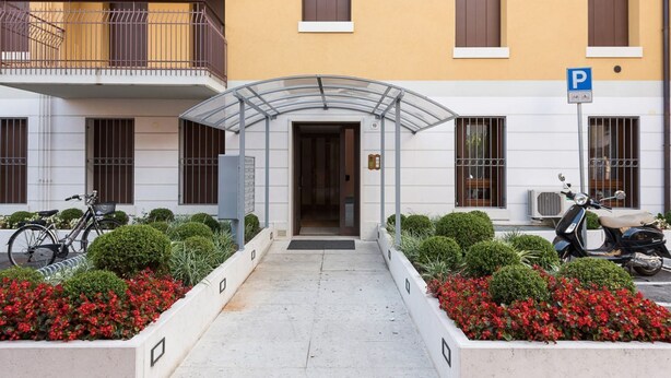 Une entrée d’immeuble avec un passage couvert, un panneau indiquant l’emplacement du parking et un scooter garé à l’extérieur.