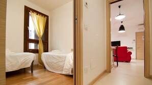 Une chambre avec deux lits, un plancher en bois, un bureau avec une chaise et une chaise rouge.