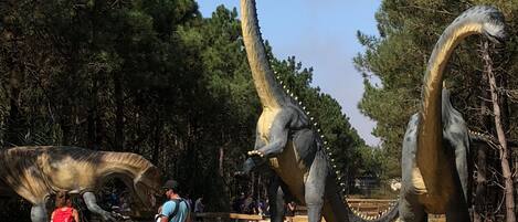 A dinosaur exhibit with large models of sauropods, a wooden fence, and visitors observing the displays.