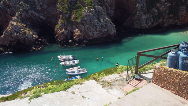 Une zone côtière où des bateaux sont amarrés près de falaises rocheuses, et un escalier descend vers la mer.