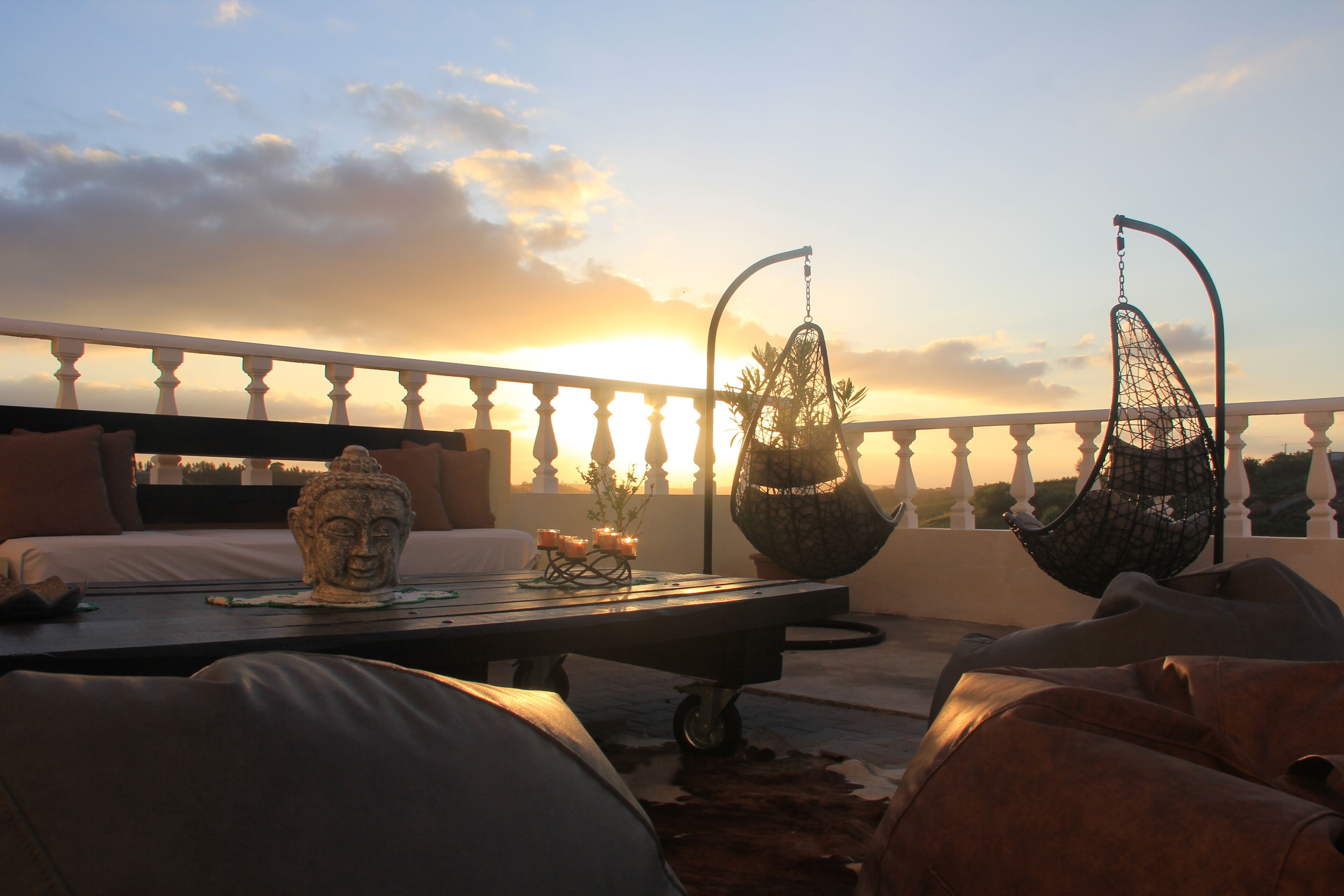 Ein Balkon mit Bett, Hängestühlen und einer Buddha-Statue.