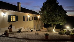 Un bâtiment doté de nombreuses fenêtres, dont certaines sont équipées de volets, et d’un grand arbre qui se trouve devant.