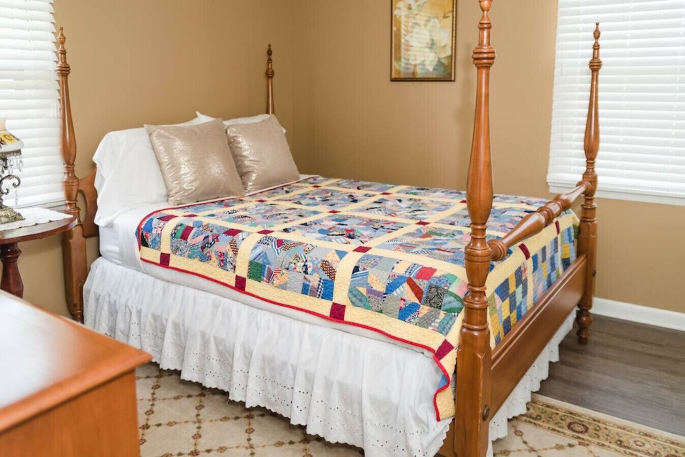 Een hemelbed met een kleurrijke quilt, witte lakens en een kantboord.