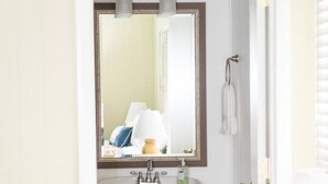 A bathroom with a pedestal sink, a mirror, and a door leading to another room.