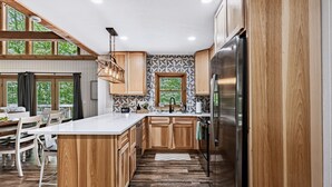 A modern kitchen with wooden cabinetry, a central island, and a built-in refrigerator. - Freshly Remodeled Cabin Escape—Hot Tub, Treehouse, Game Room, WiFi, 2 Decks (Rockbridge)