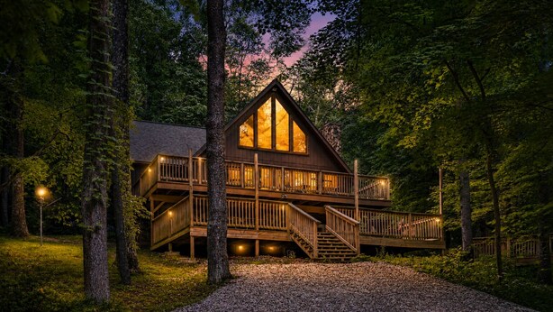 A cabin with a wooden exterior, a balcony, and a staircase leading to the entrance. - Freshly Remodeled Cabin Escape—Hot Tub, Treehouse, Game Room, WiFi, 2 Decks (Rockbridge)