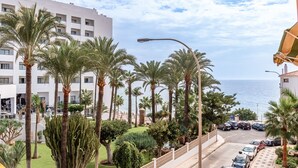 Un hotel con vistas al mar, palmeras y coches estacionados.