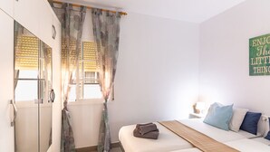 Un dormitorio con cama, mesita de noche, espejo y ventana con cortinas.
