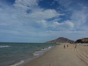 A beach with people, a mountain, and a clear sky.