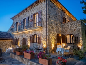 Un edificio de piedra con varios balcones, mobiliario exterior y un patio bien iluminado.