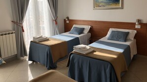 A hotel room with two beds, a radiator, a painting, and a window with curtains. - Family Room for 3-4 pers (Dese)