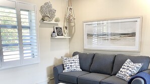Una sala de estar con un sofá gris, cojines estampados, una mesa de centro blanca y un cuadro enmarcado en la pared.
