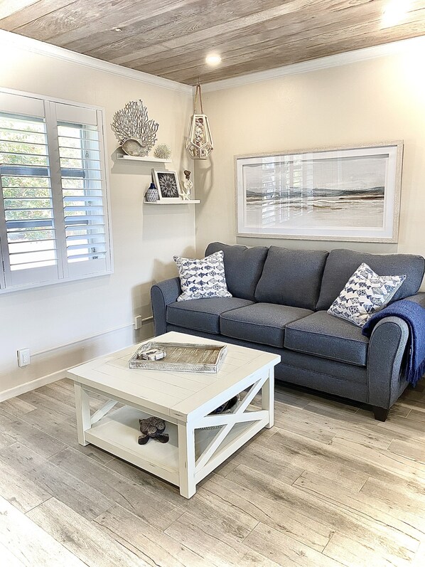 A living room with a grey sofa, patterned cushions, a white coffee table, and a framed picture on the wall.