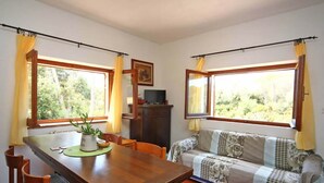 A room with a wooden dining table, chairs, a sofa, and a television on a cabinet. - Villa Paradisino Orbetello, Bilocale Flamingo B (Orbetello)